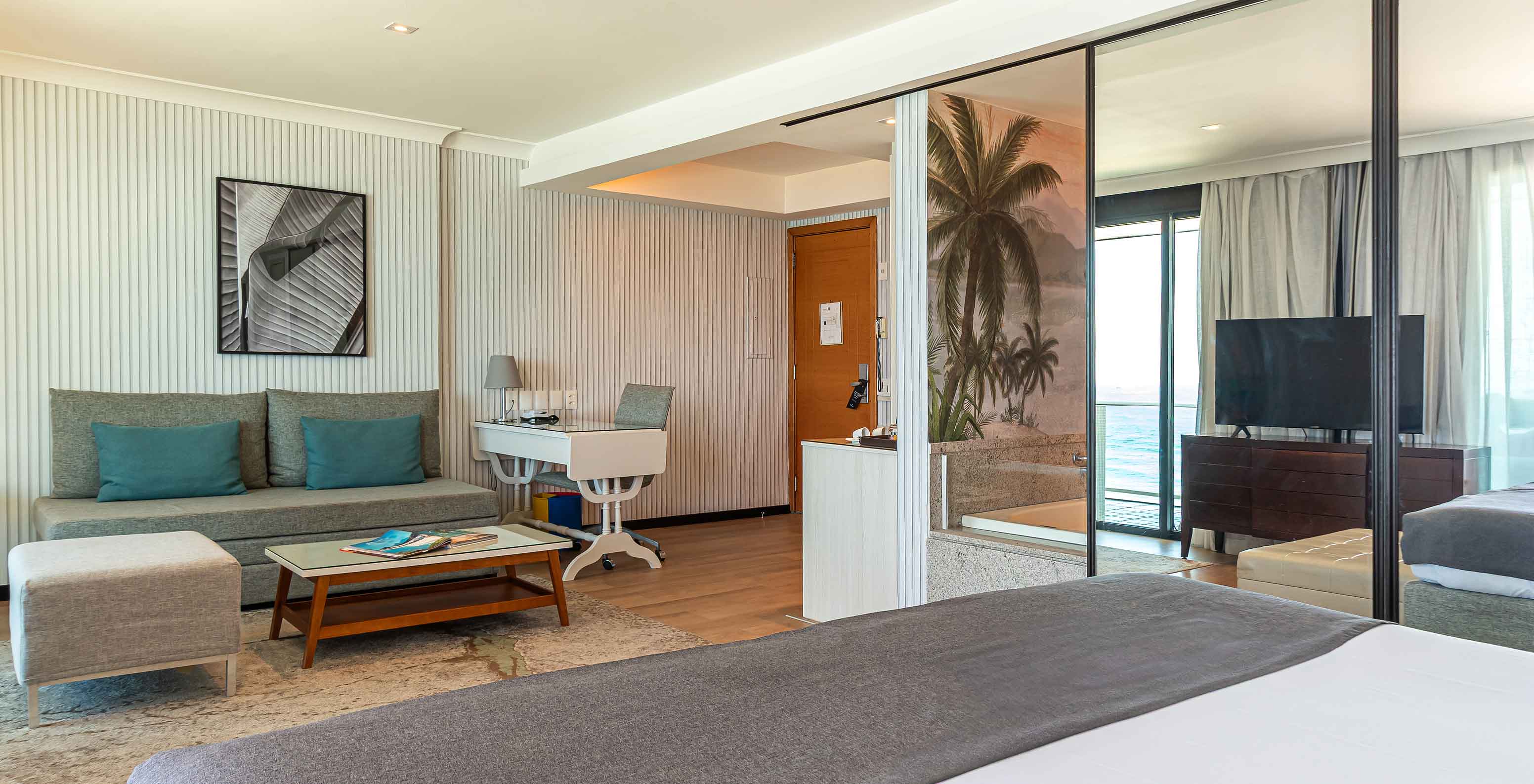 The Suite Beach Front at Pestana Rio Atlântica has a modern room with bed, sofa, table and TV.