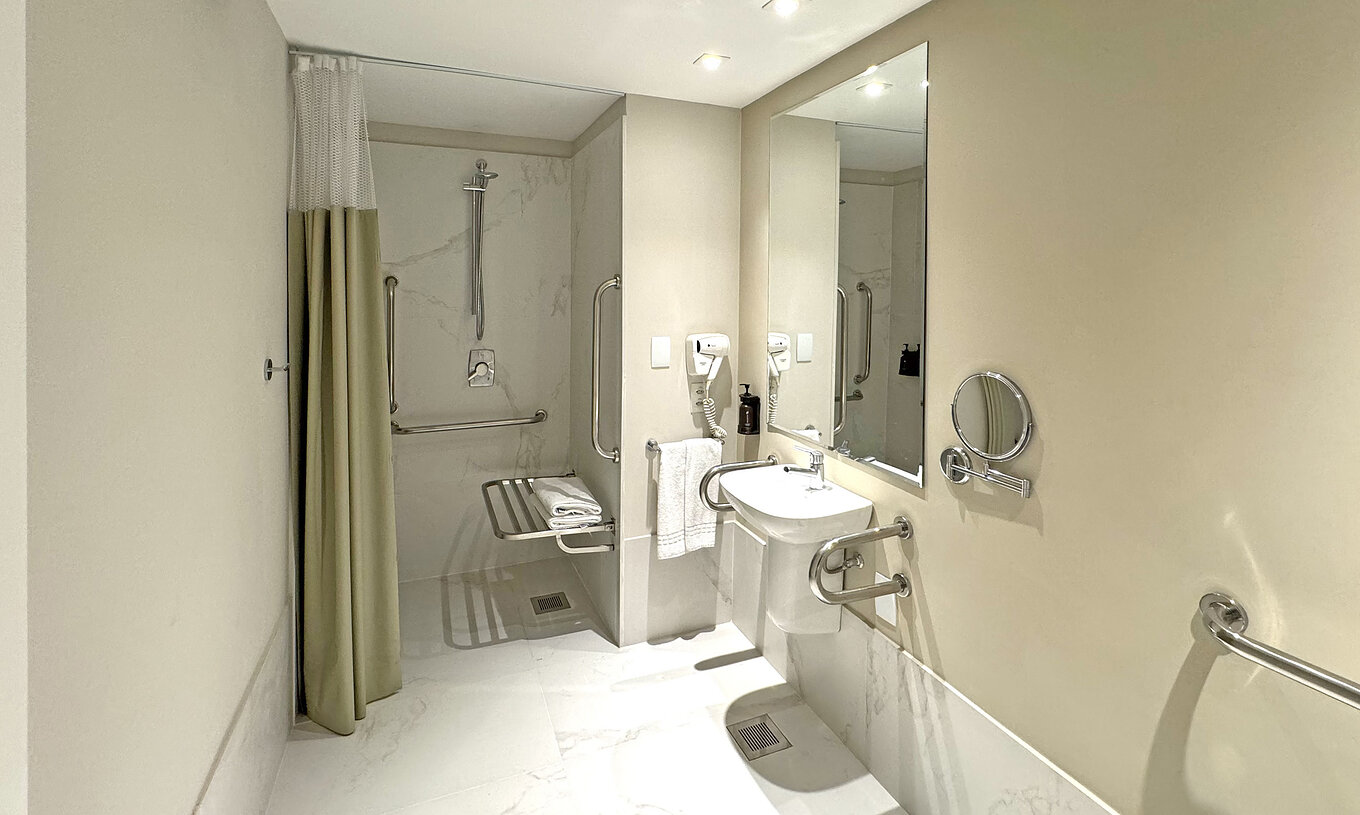 The Queen Disable Standard of Pestana Rio Atlântica has an adapted bathroom with shower, sink, mirror, and hairdryer