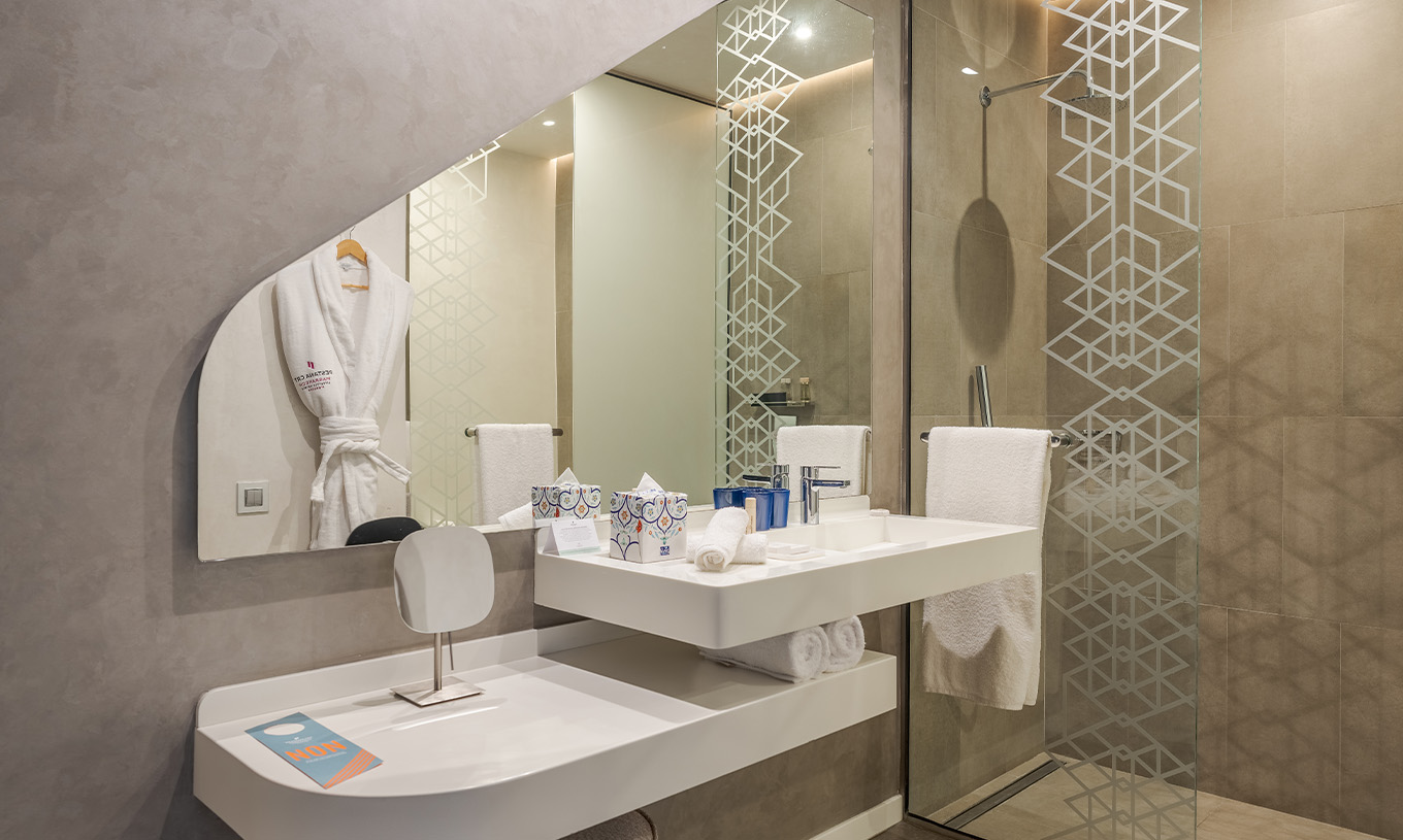 The CR7 Junior Suite at Pestana CR7 Marrakech has a bathroom with a walk-in shower, sink with mirror, and shelf