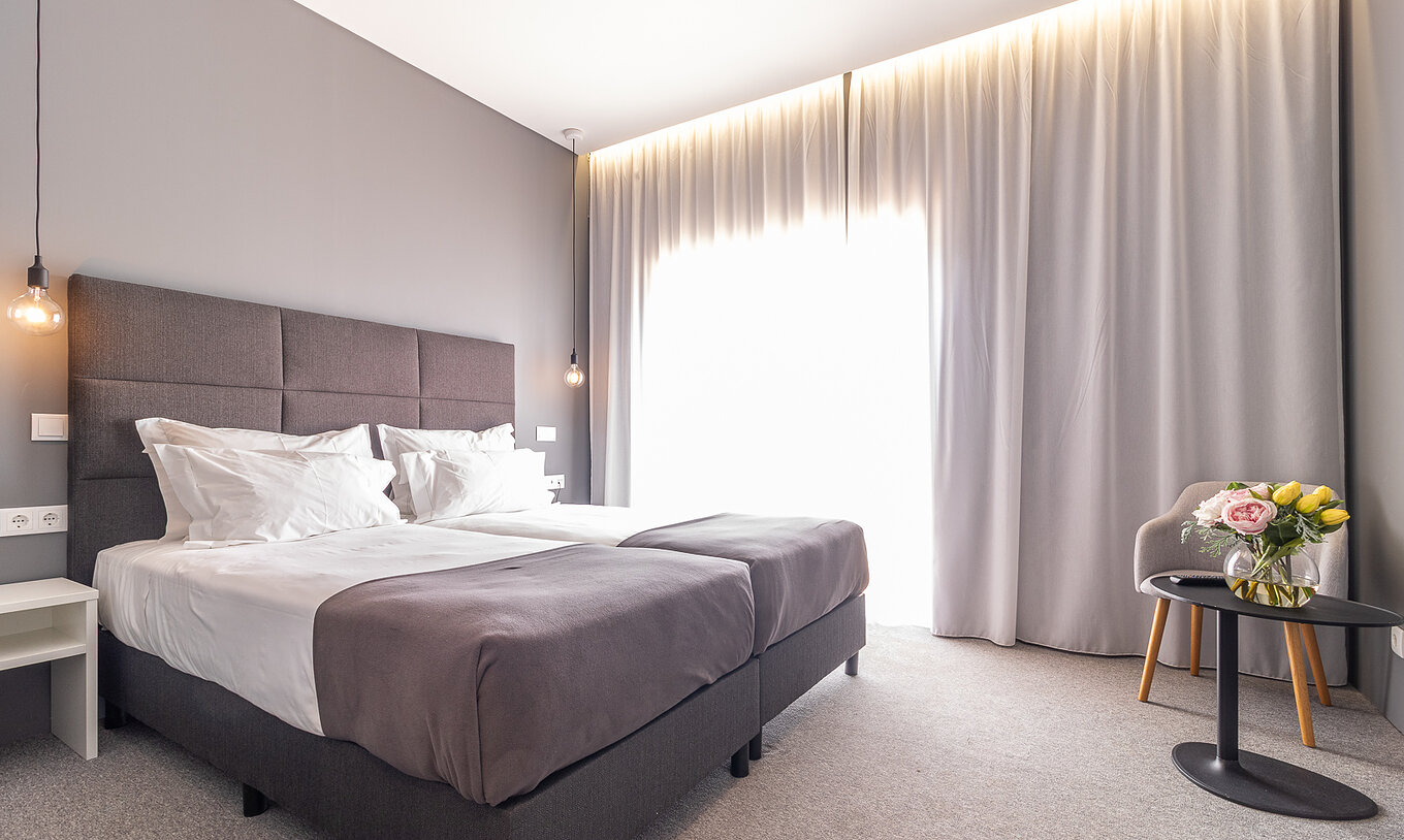 The Classic Pool View Room at Pestana Gramacho is modern with two beds, grey curtains and a table with flowers