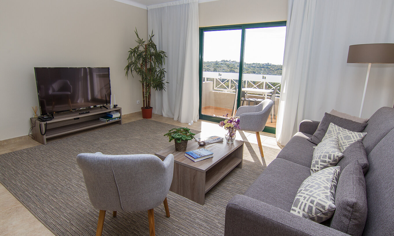 The T2 Apartment at Pestana Gramacho Residences includes a living room with a sofa, television, and a window with a balcony