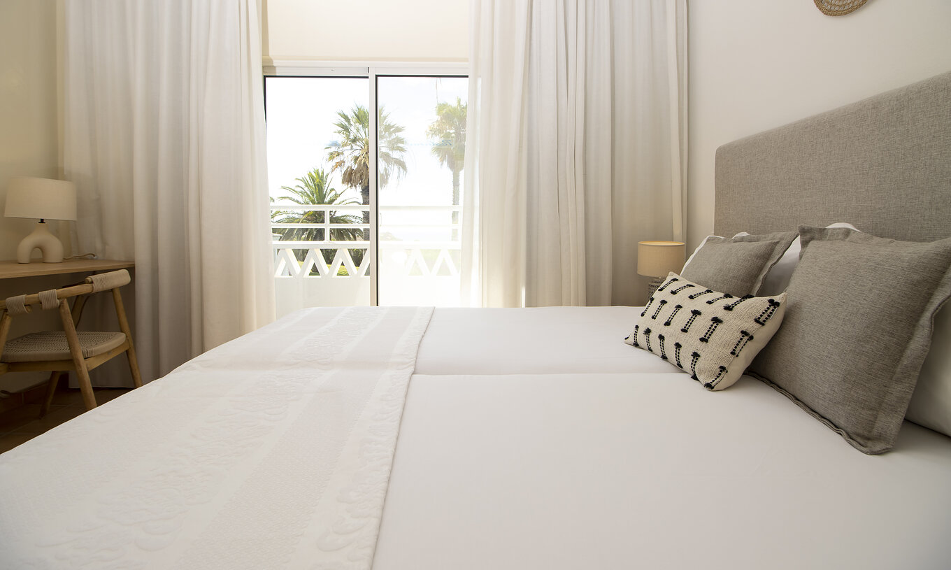 The T2 Apartment Superior do Pestana Palm Gardens has a bed with cushions, a window leading to a balcony