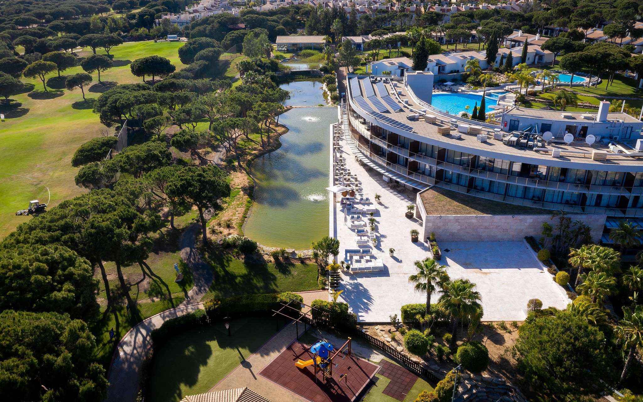 View of Pestana Vila Sol - Vilamoura, a 5-star hotel in Vilamoura with a pool and surrounded by a lake and green vegetation