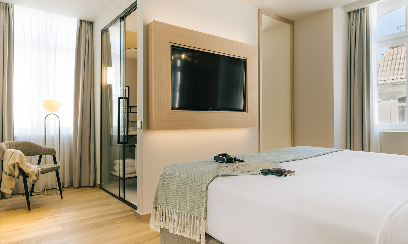 The Premium Corner of Pestana Rua Augusta Lisboa has a bed with television in front and a bathroom with glass door