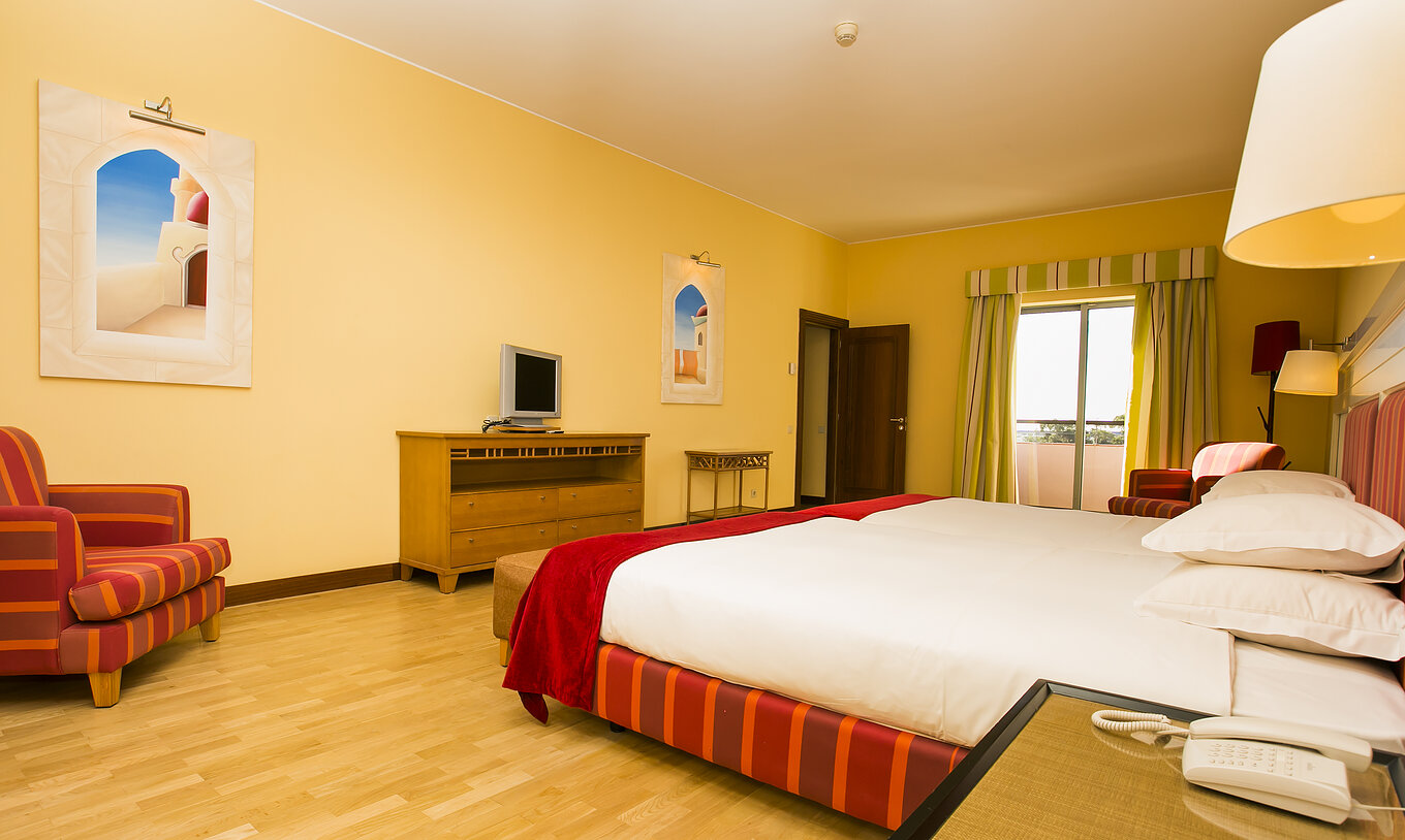 The Deluxe Mezzanine Suite of Pestana Sintra Golf has two beds, a small television, and a window with balcony access