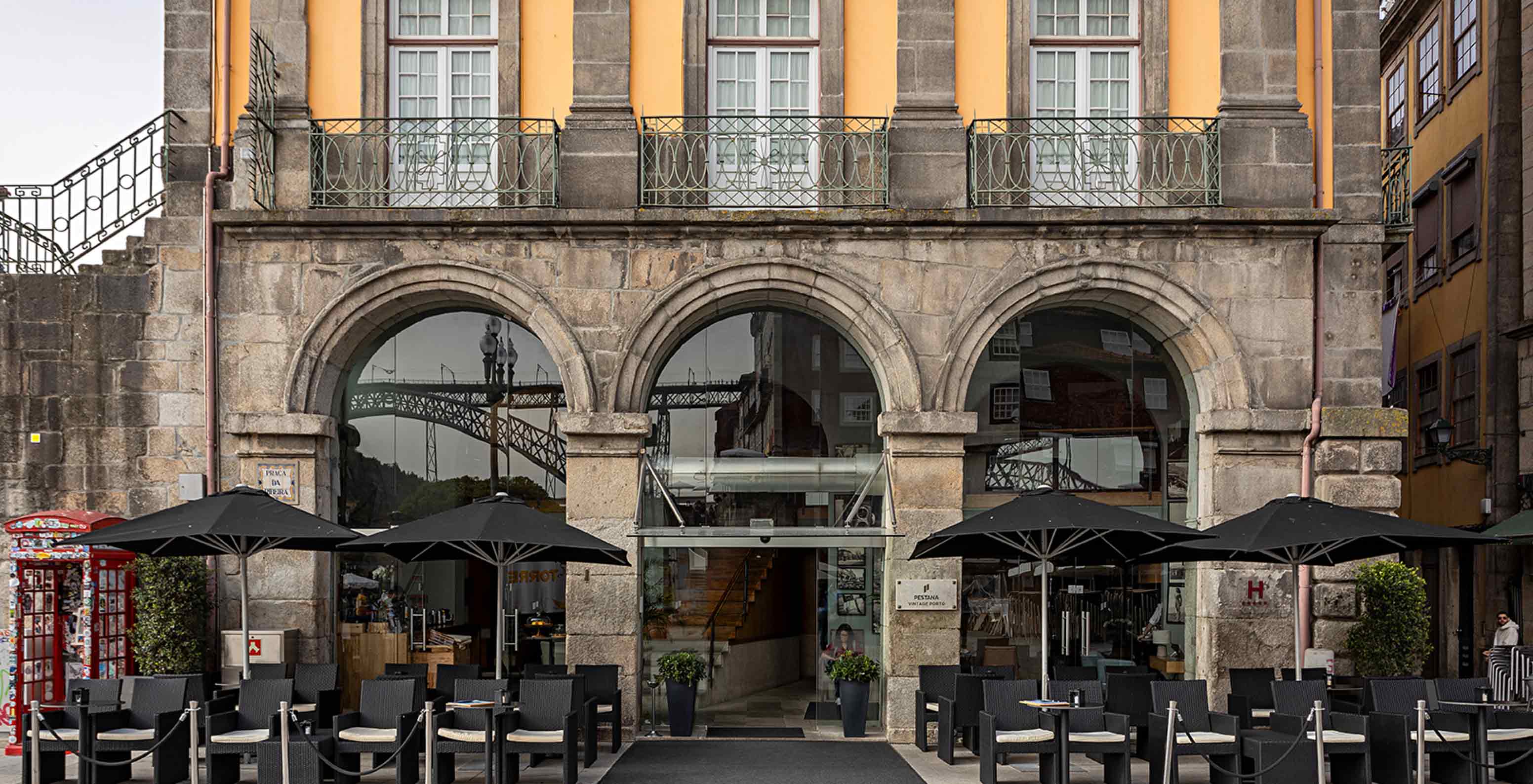 Exterior façade of Pestana Vintage Porto with access to a patio that has tables with chairs and sun umbrellas
