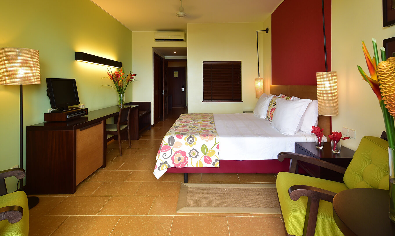 The Sea View Room of Pestana São Tomé has two single beds together, two armchairs, and a desk with a television
