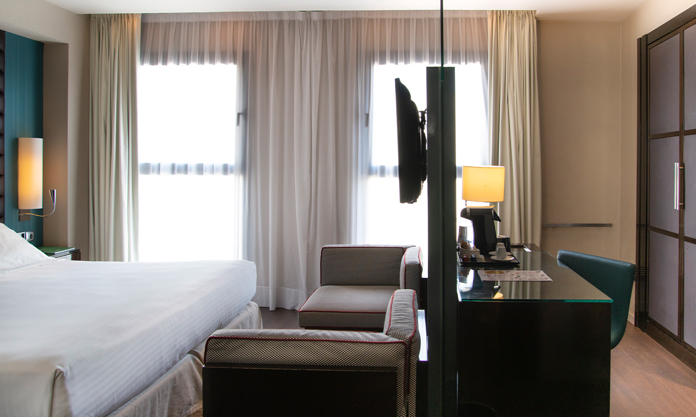 Deluxe room at Pestana Arena Barcelona has two small sofas, a TV and a desk with amenities
