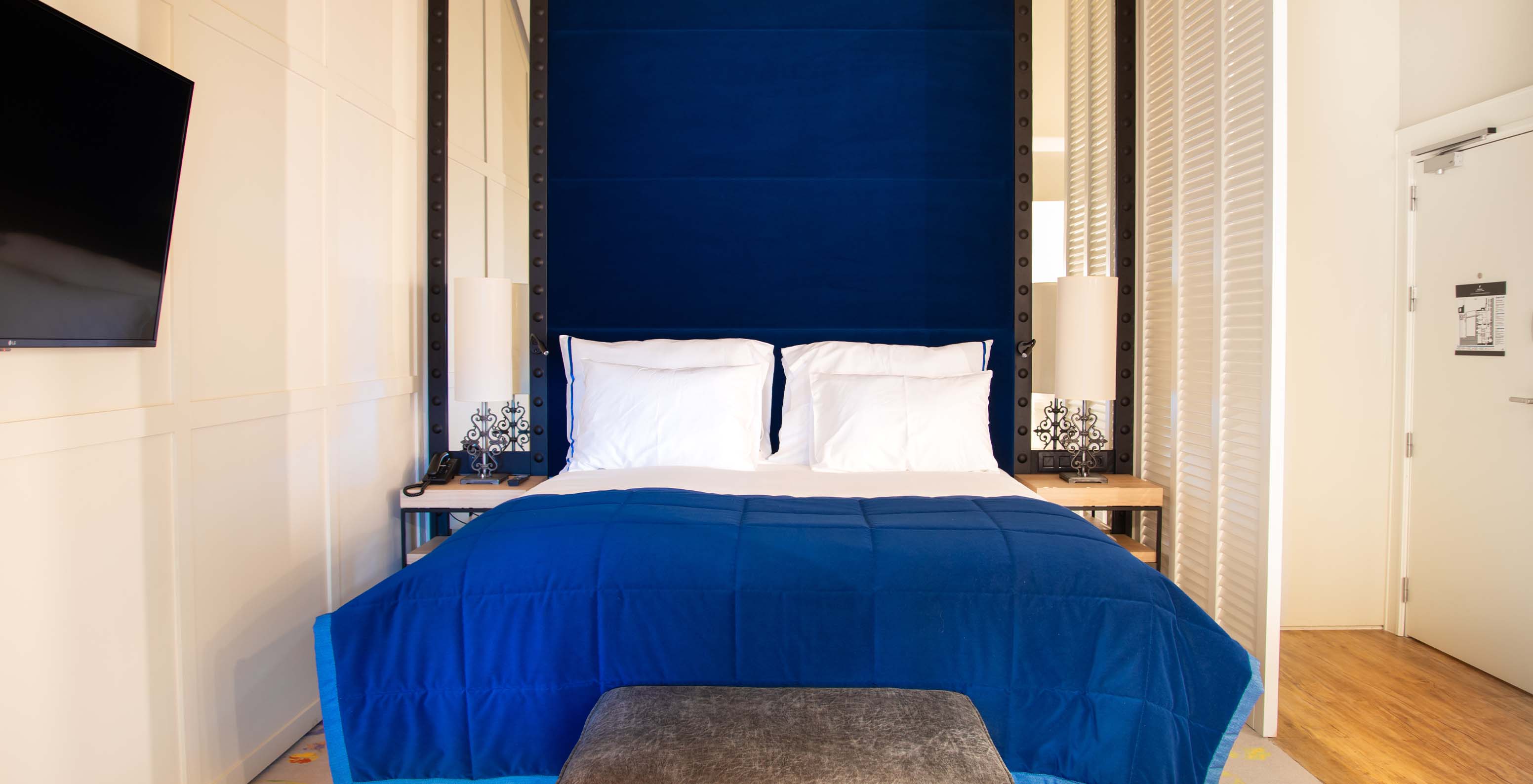 The Loft at Pestana Collection Plaza Mayor has a double bed with a blue headboard and mirrors, and a TV on the wall