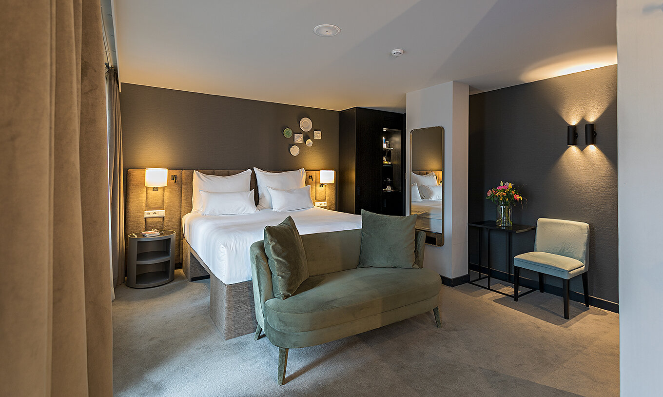 Deluxe room at Pestana Amsterdam Riverside has a double bed, bedside table, and a sofa in front of the bed