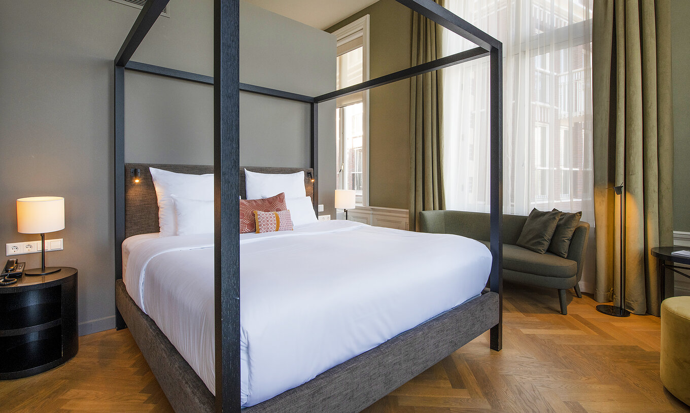 Junior Suite - River View at Pestana Amsterdam Riverside has a double bed with canopy and a green sofa