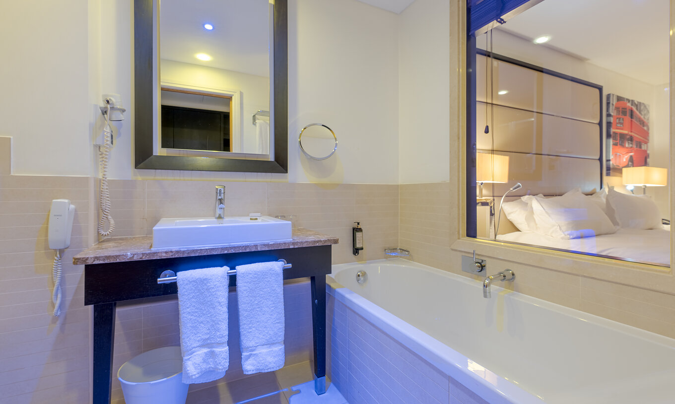 The Premium Twin at Pestana Chelsea Bridge has a bathroom with bathtub, glass wall, sink, mirrors and hairdryer