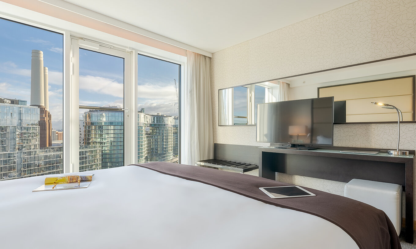 The Superior King at Pestana Chelsea Bridge has double bed, desk with TV, sofa and windows facing the city