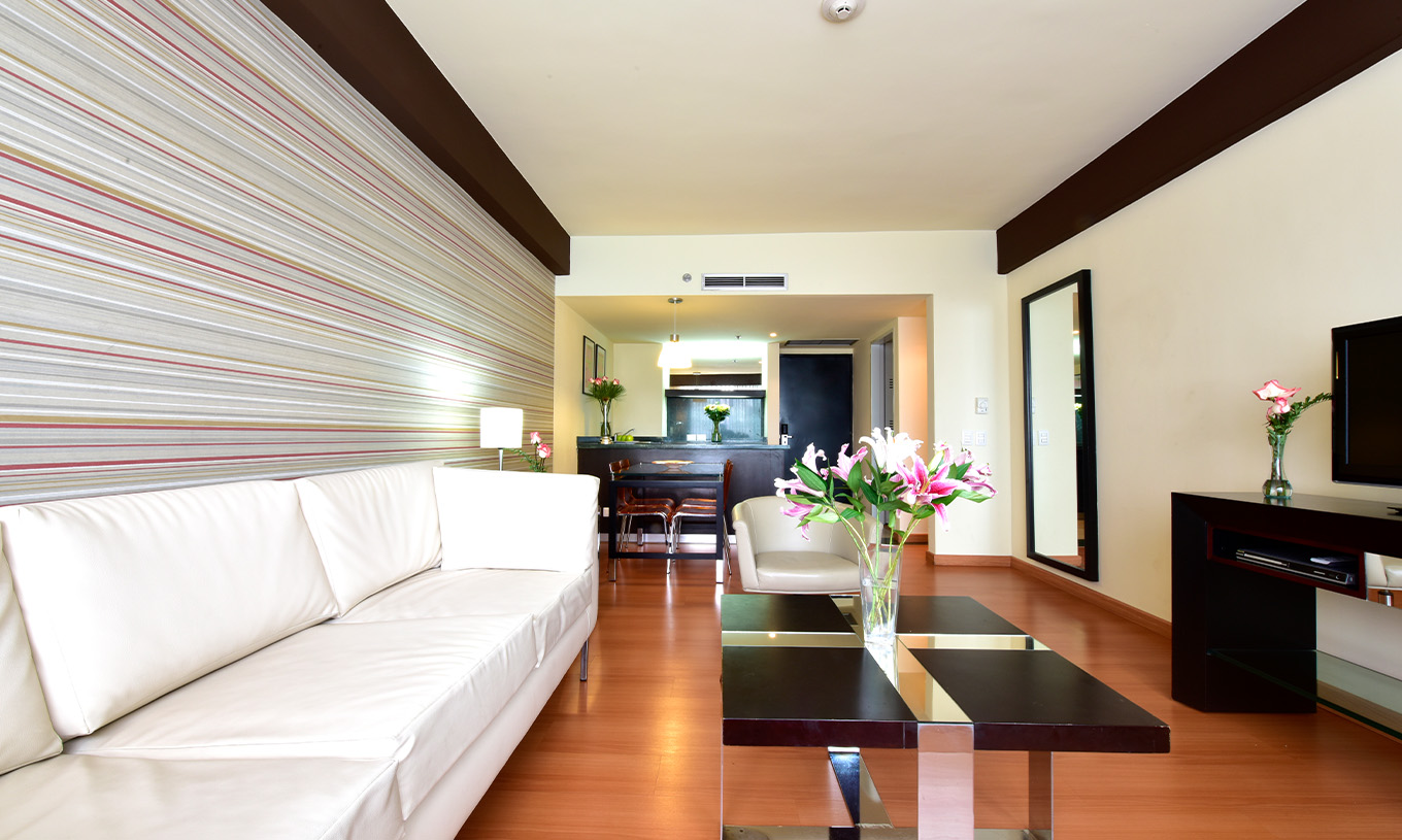 The Twin Junior Suite at Pestana Caracas has a living room with a two-seater white sofa, a TV, and a side table