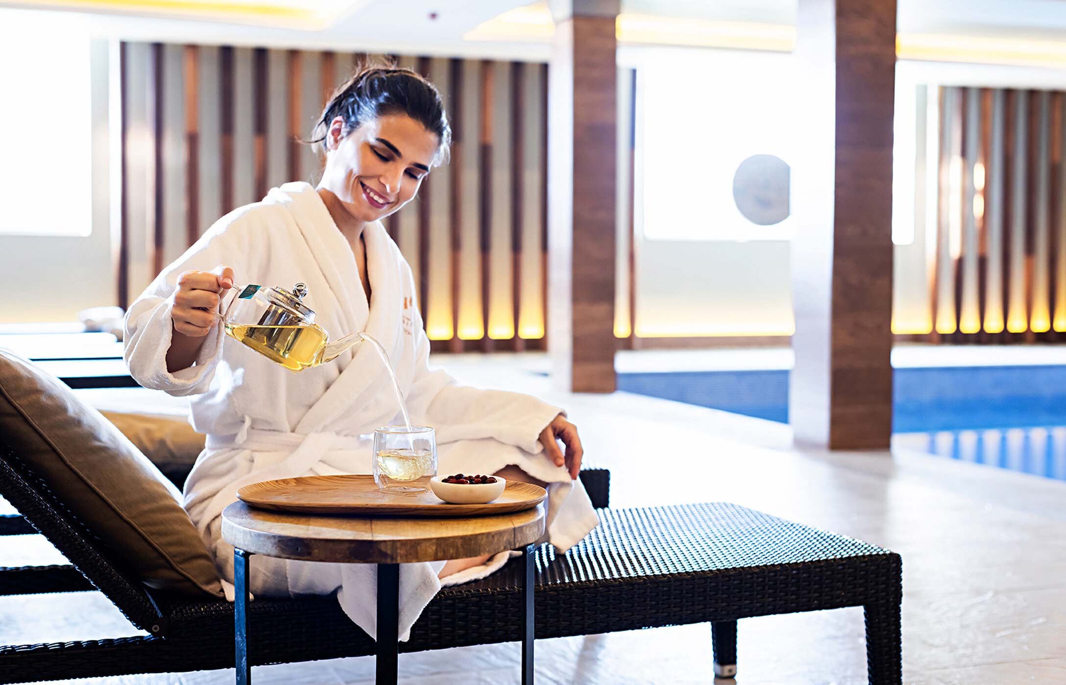 A guest drinking tea on a lounge chair by the indoor pool at Palácio do Freixo Spa, with modern decor