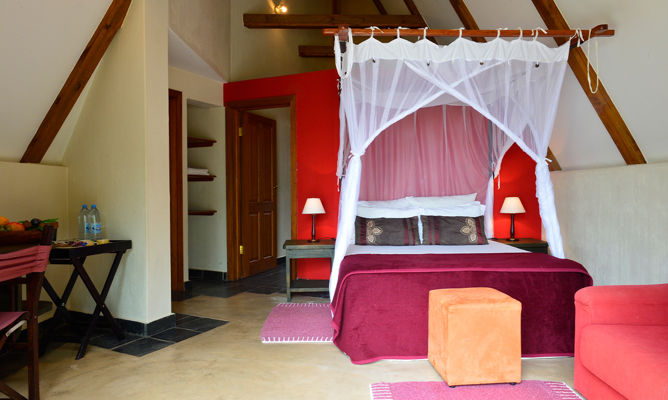El Bungalow T1 del Pestana Bazaruto Lodge tiene decoración en tonos rojos con cama doble, sofá y escritorio
