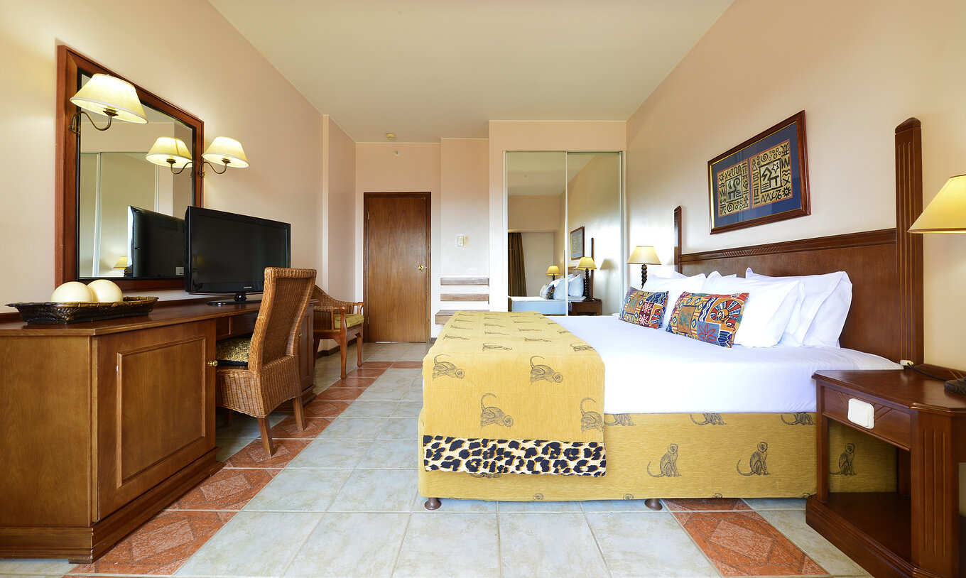 La Suite Luxo del Pestana Rovuma tiene una cama y un cuadro con decoración típica africana, un escritorio y televisión