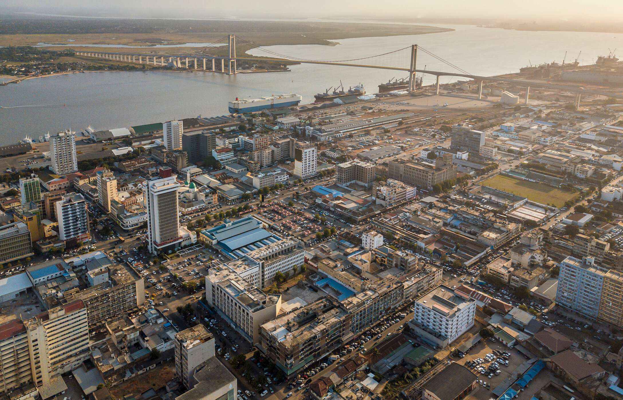 Vista aérea de la ciudad de Maputo, Mozambique, con varios edificios, coches y un puente sobre un río.