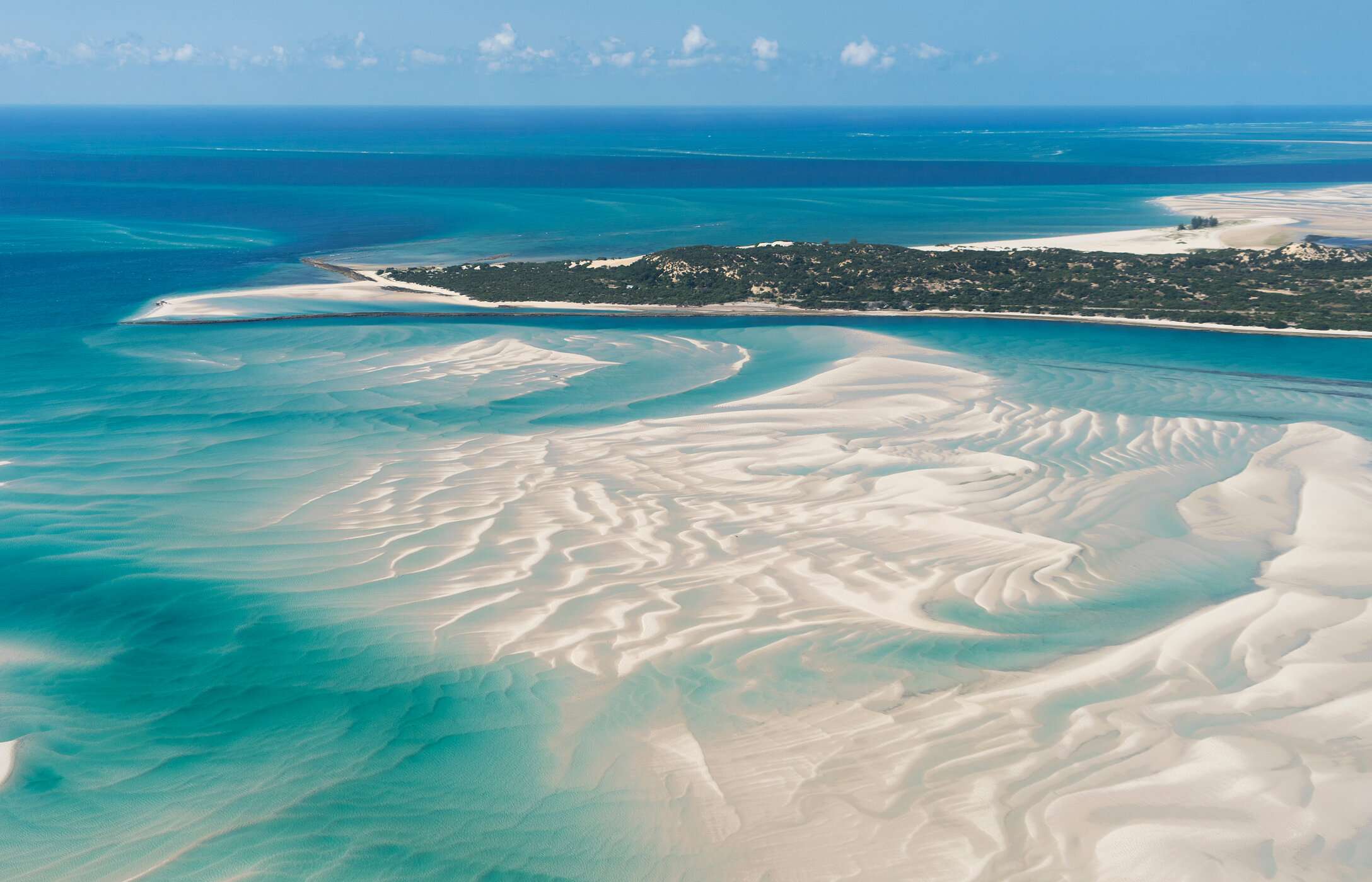 Vista aérea de la isla Vilankulo, Mozambique, con aguas cristalinas, varios bancos de arena en el mar y vegetación al fondo.