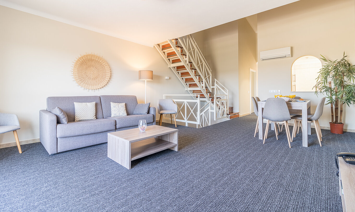 El apartamento de dos dormitorios en Pestana Gramacho tiene salón con sofá gris, mesa y escaleras al fondo