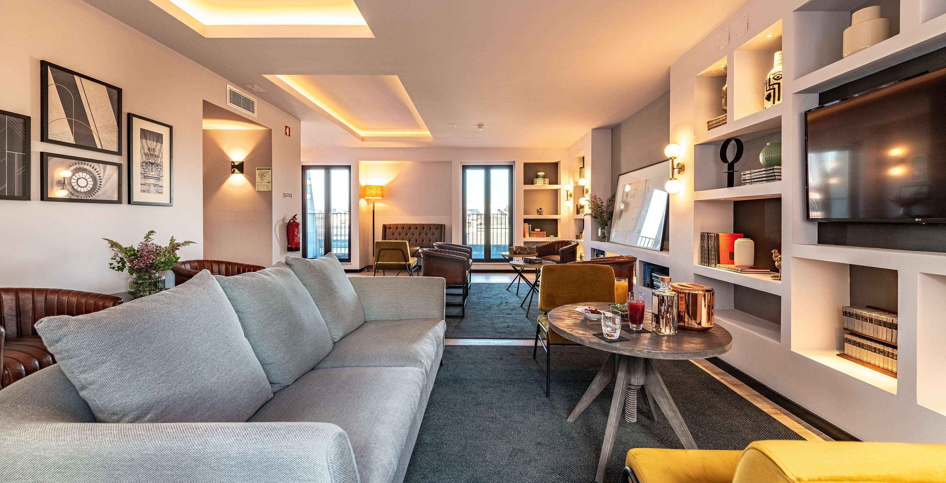 Lounge con sofás, sillas, mesas, cuadros, televisión, alfombras y objetos de decoración con ventanas con vista a la ciudad