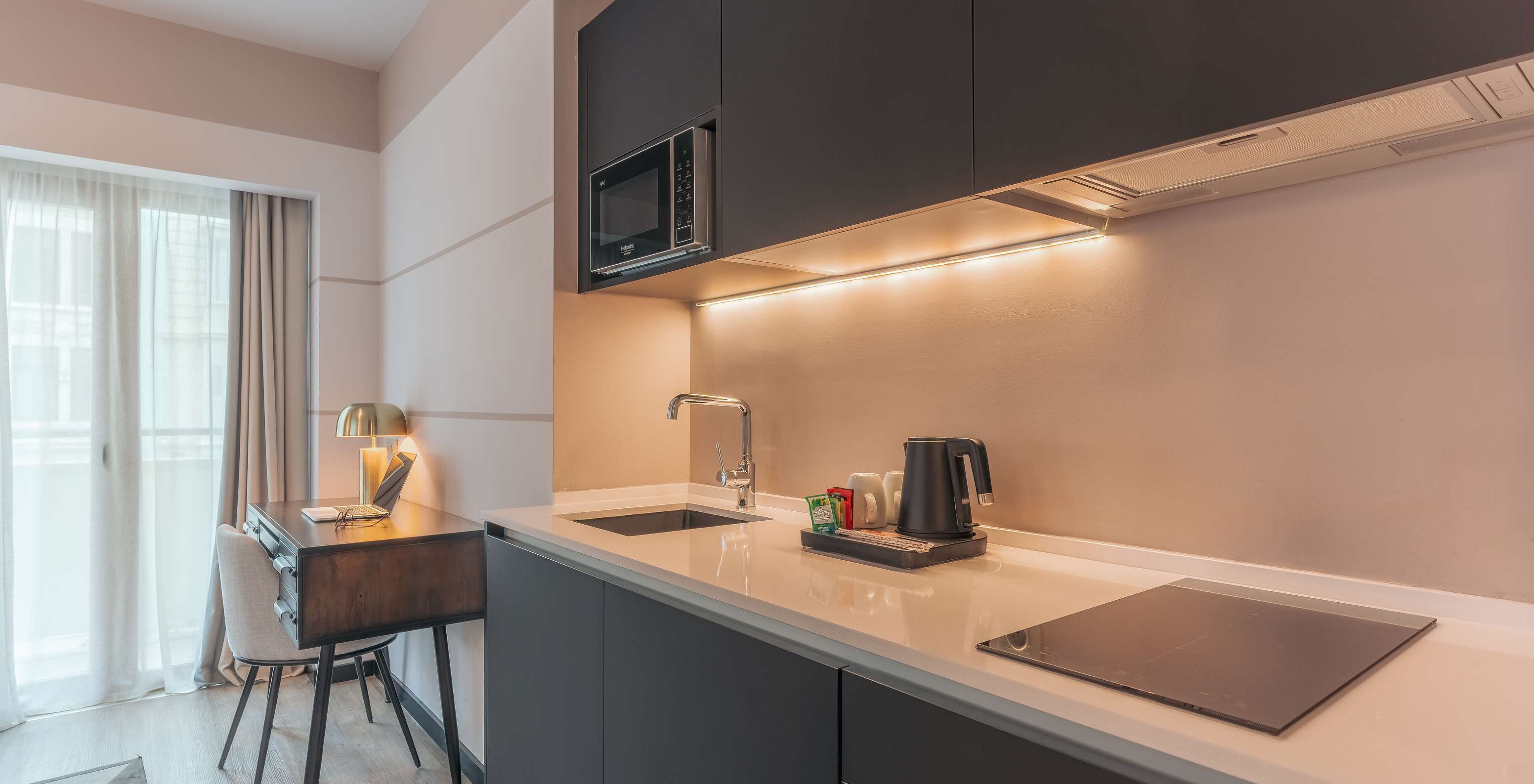 La Junior Suite del Pestana Lisboa Vintage tiene un mueble de cocina con placa de fogón, microondas y un escritorio con silla