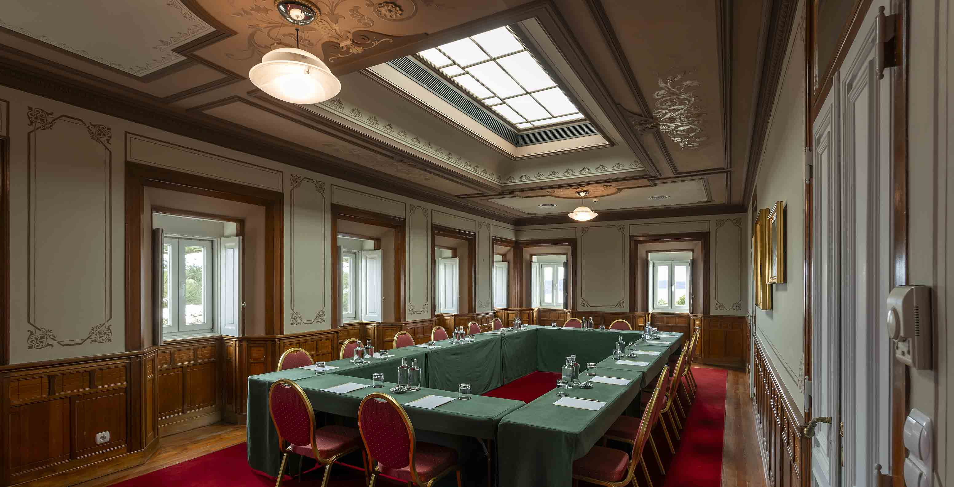 El Pestana Palace Lisboa tiene una sala de reuniones con una mesa rectangular, rodeada de ventanas, incluyendo en el techo