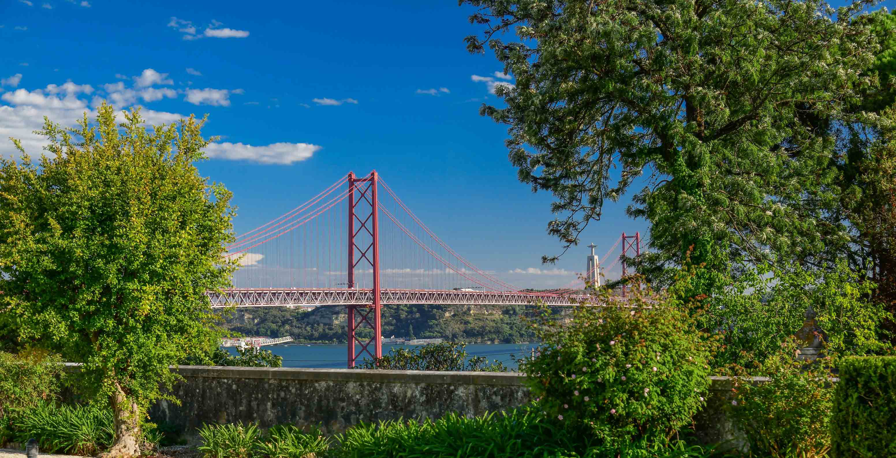 Vista del Pestana Palace Lisboa hacia el puente 25 de Abril y el Río Tajo, con varios edificios y árboles por el medio