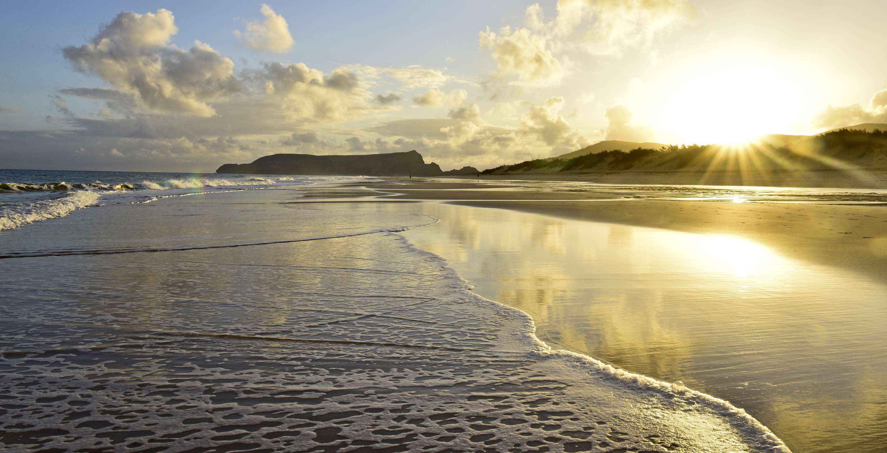 Atardecer en la playa de Porto Santo, con cielo repleto de nubes anaranjadas y el sol lanzando sus rayos dorados sobre el mar