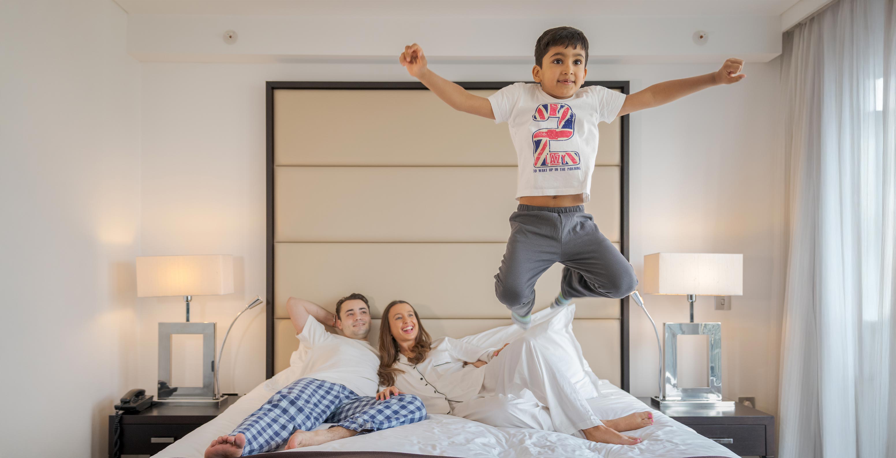 El Deluxe Family del Pestana Chelsea Bridge tiene cama doble con familia acostada y un niño saltando
