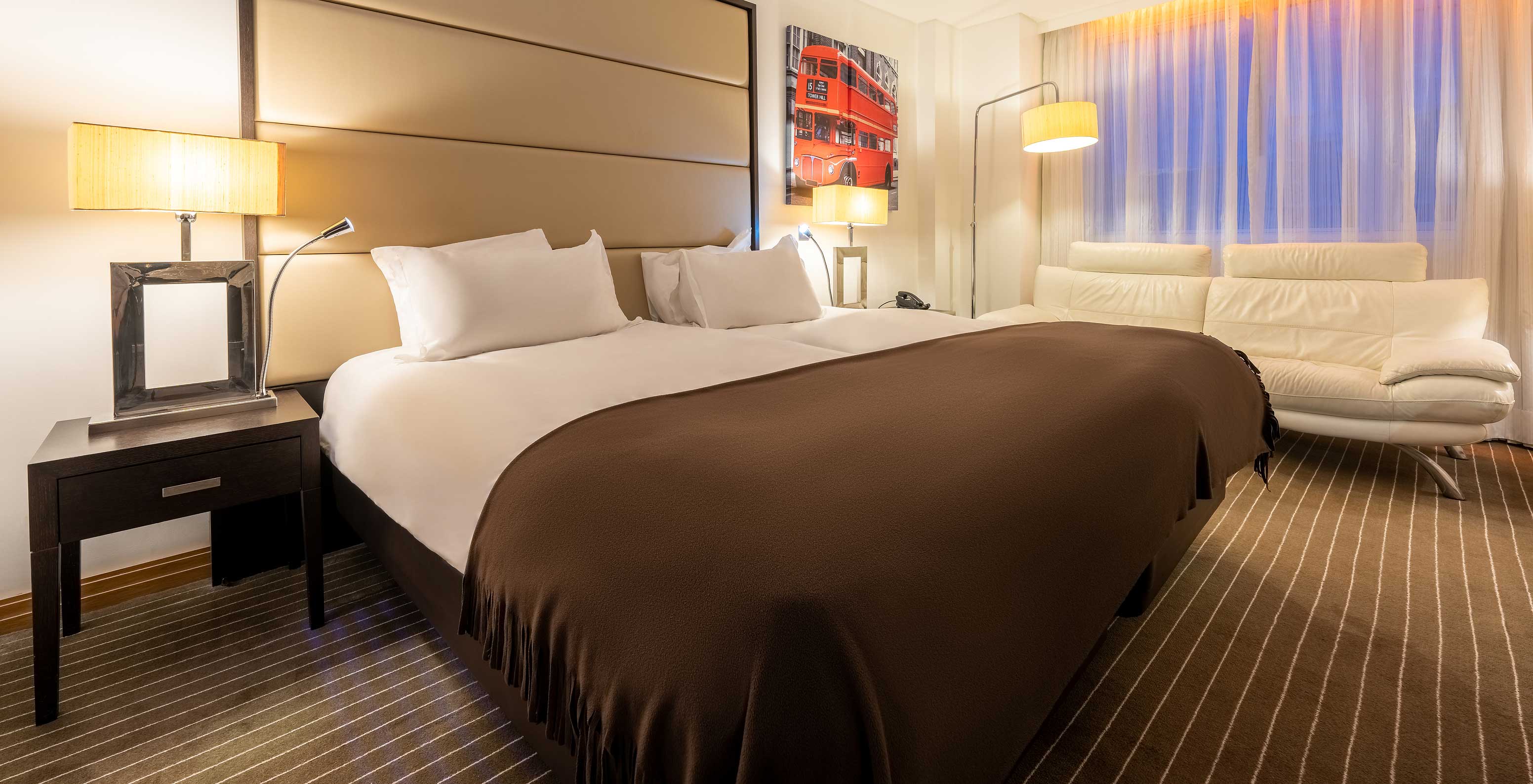 El Premium Twin del Pestana Chelsea Bridge tiene dos camas juntas, mesa de noche, sofá, lámparas y ventanas con cortinas