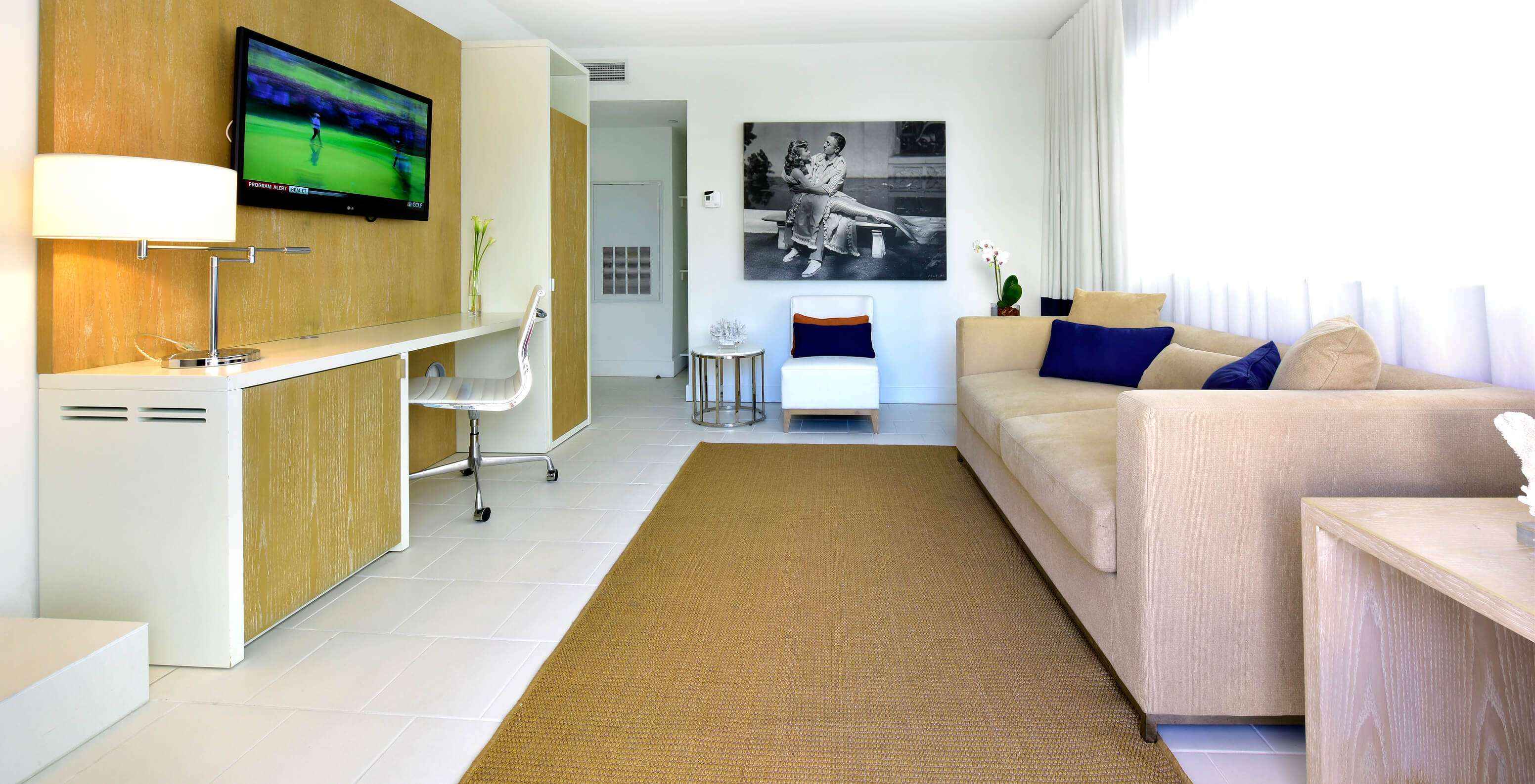La Suite de dos dormitorios con balcón del Pestana Miami South Beach cuenta con sala con sofá, silla, televisor y un escritorio