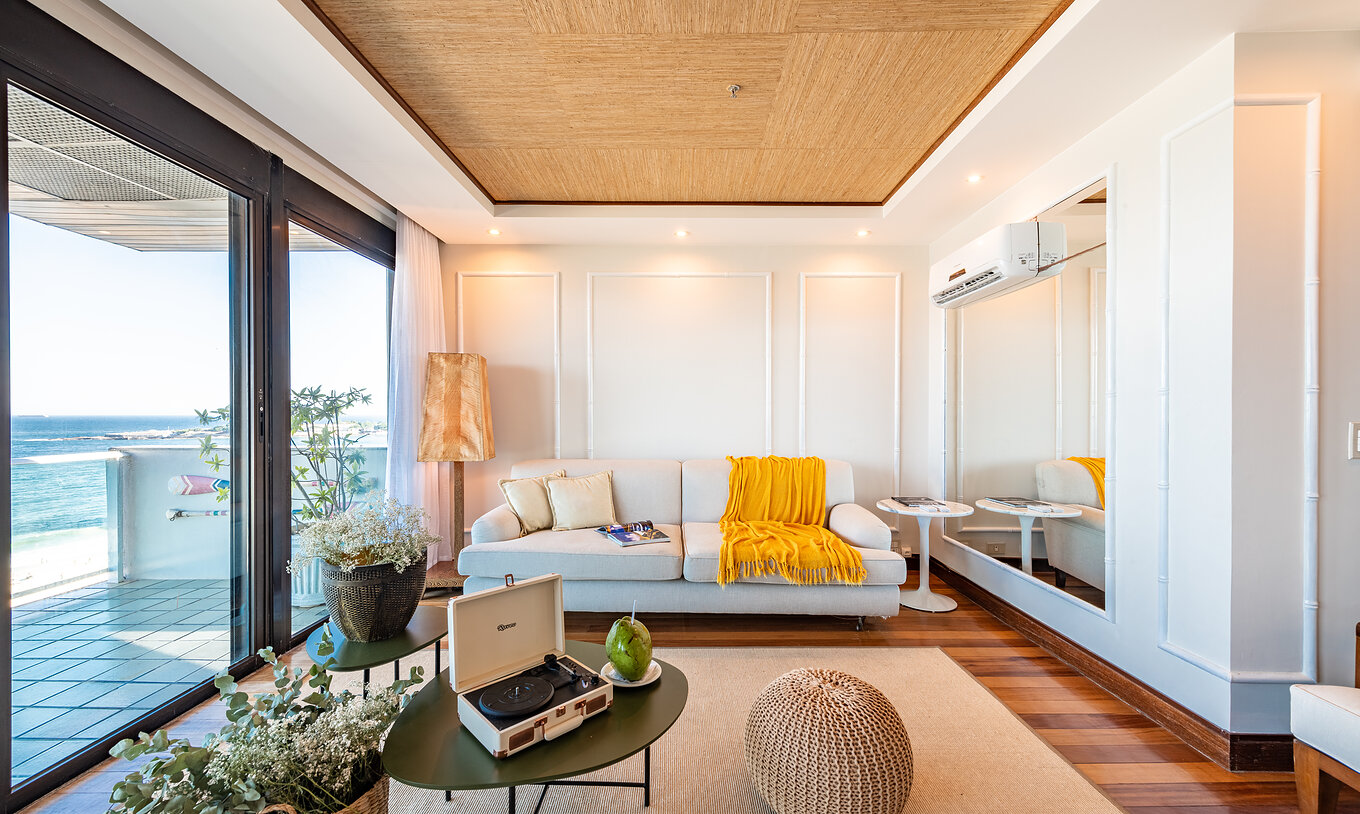 La Suite Presidencial del Pestana Rio Atlântica tiene una sala con techo de madera, sofá blanco y vista al mar