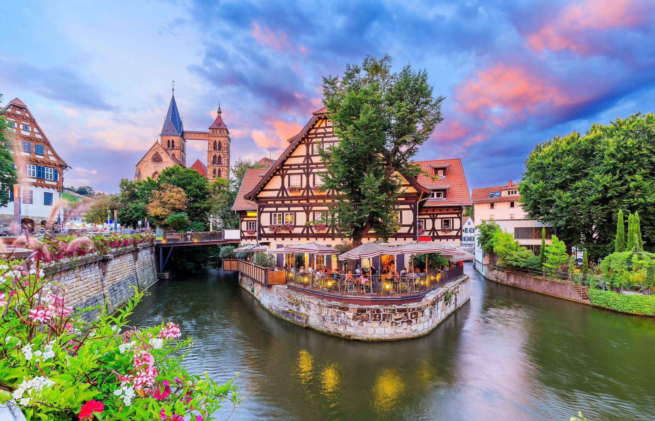 Una encantadora ciudad medieval en Alemania con casas coloridas, una iglesia al fondo y un puente sobre un río.
