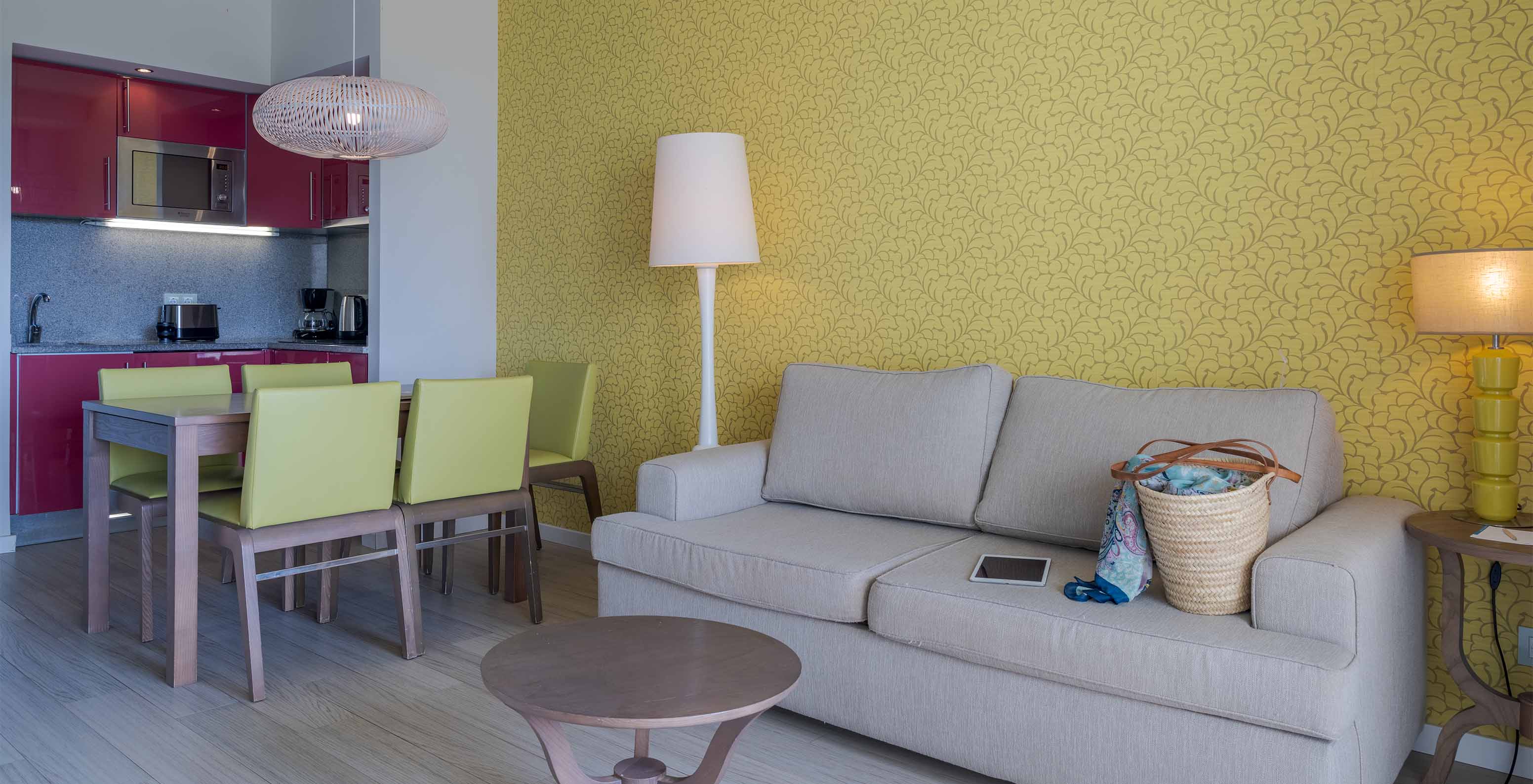 La Suite T1 Vista Jardín del Pestana Alvor Praia tiene mesa de comedor con cinco sillas verdes y sofá con mesa de apoyo