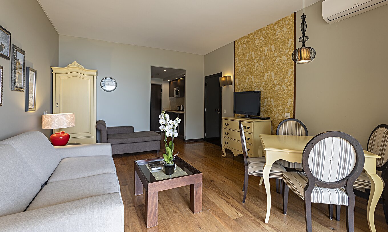 La Suite Cliff T1 en Pestana Alvor Praia tiene una sala de estar con un sofá, papel pintado, televisión y una mesa de comedor