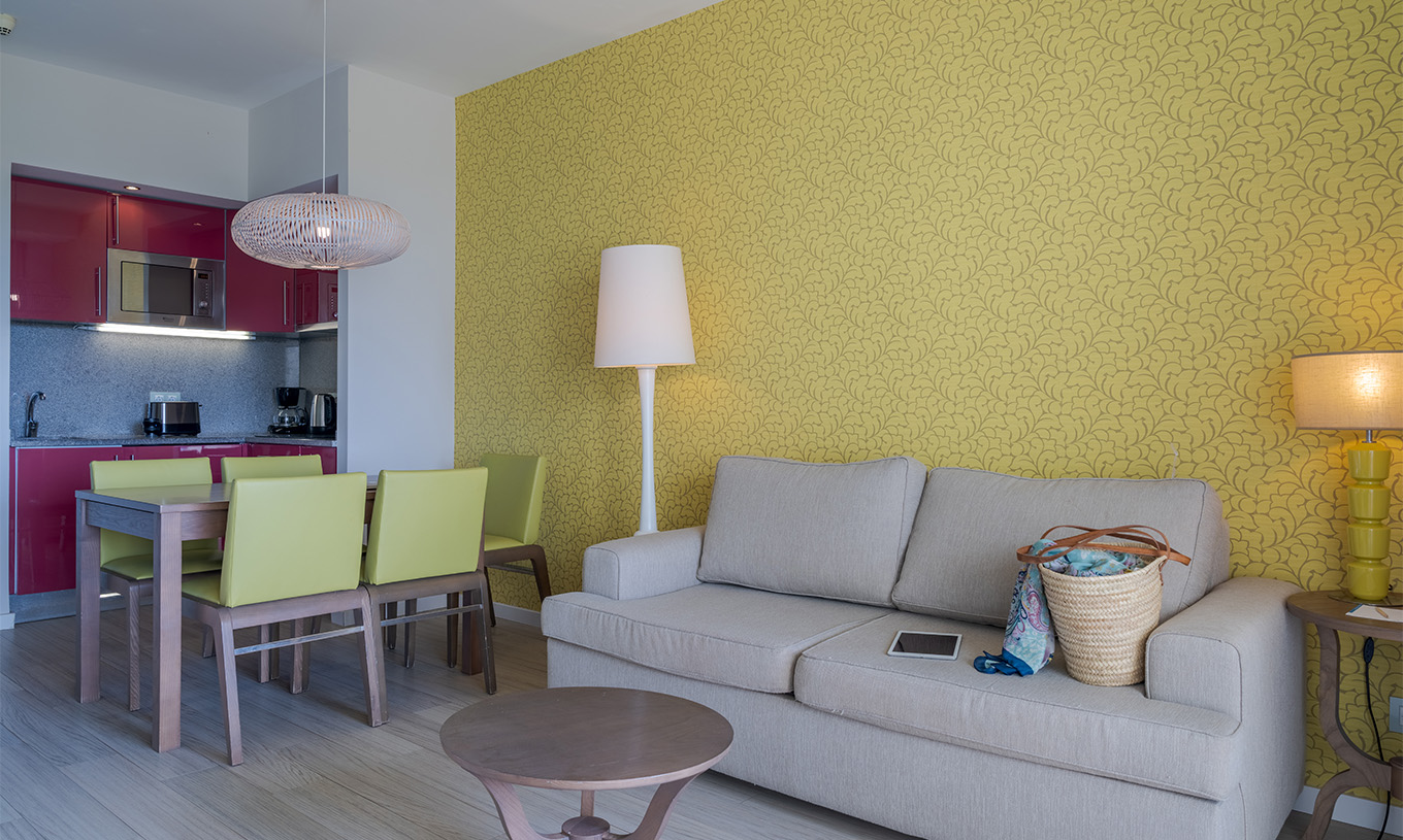 La Suite T1 Vista Jardín del Pestana Alvor Praia tiene mesa de comedor con cinco sillas verdes y sofá con mesa de apoyo