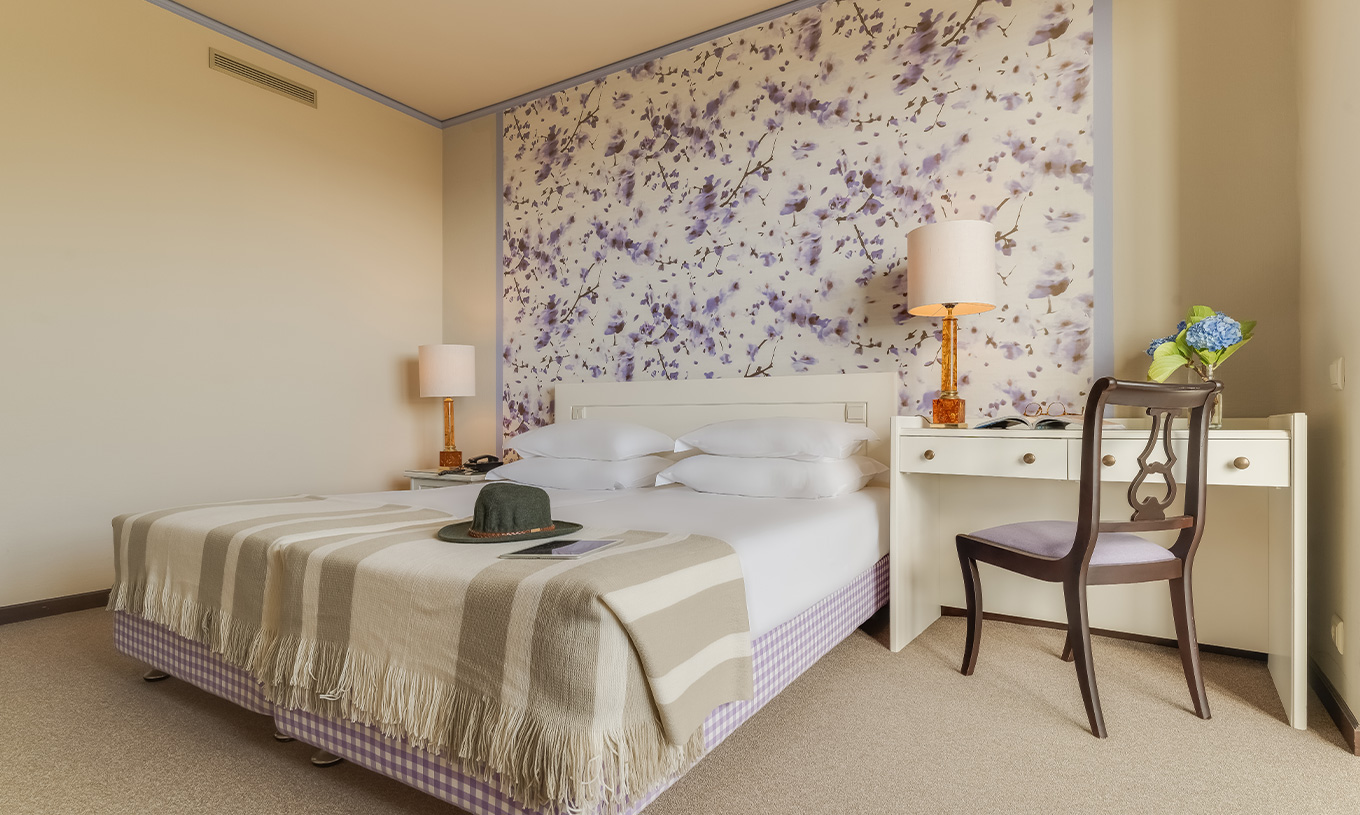 El Standard Vista Jardín del Pestana Bahia Praia tiene una cama con 4 almohadas y una mesa al lado de la cama con silla