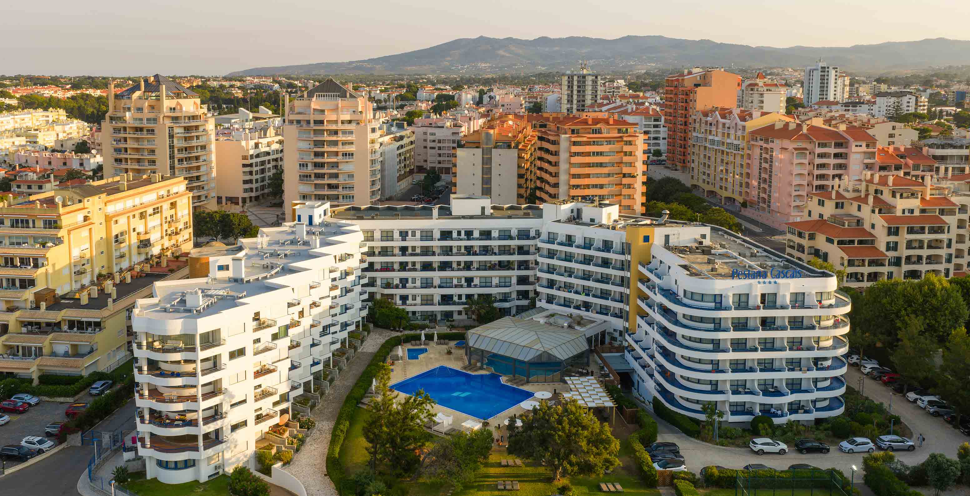 Vista aérea del hotel con los balcones, las piscinas y el jardín, y la ciudad detrás con la sierra al fondo