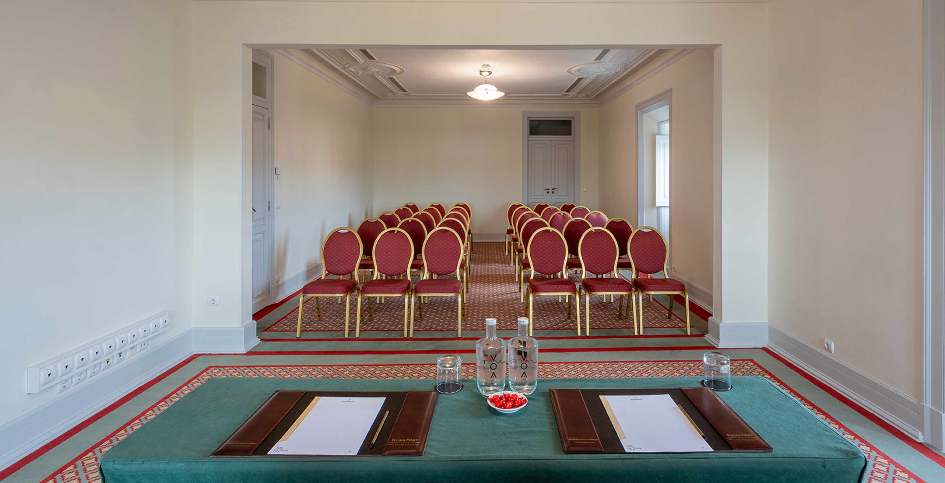 El Pestana Palace Lisboa tiene una sala de reuniones con varias sillas rojas y mesa verde rectangular