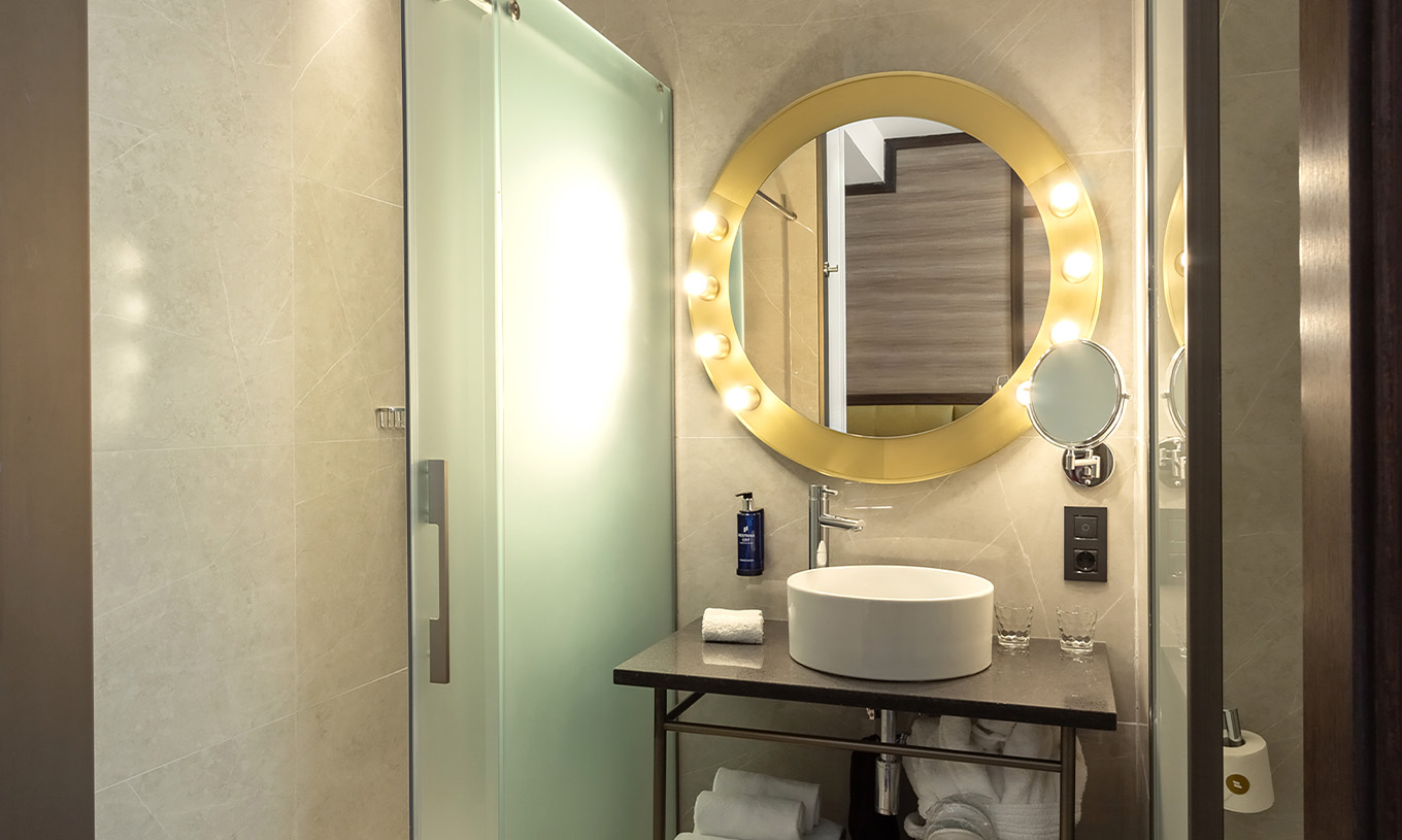 El Deluxe Grand con Vista del Pestana CR7 Gran Vía Madrid tiene un baño con un espejo, lavabo y puertas de vidrio