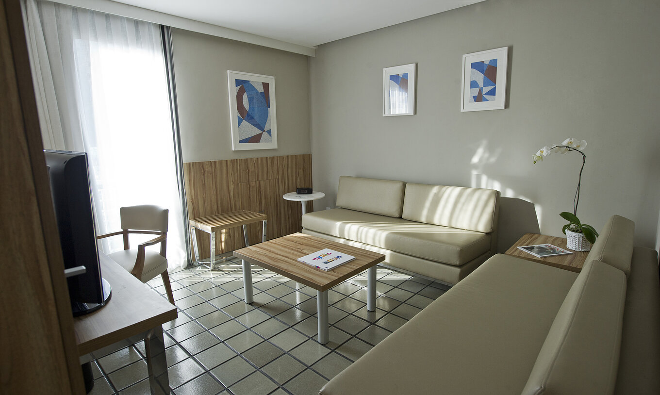 La Suite Standard du Pestana Rio Atlântica a un salon avec deux canapés beiges confortables, une table basse et une télévision