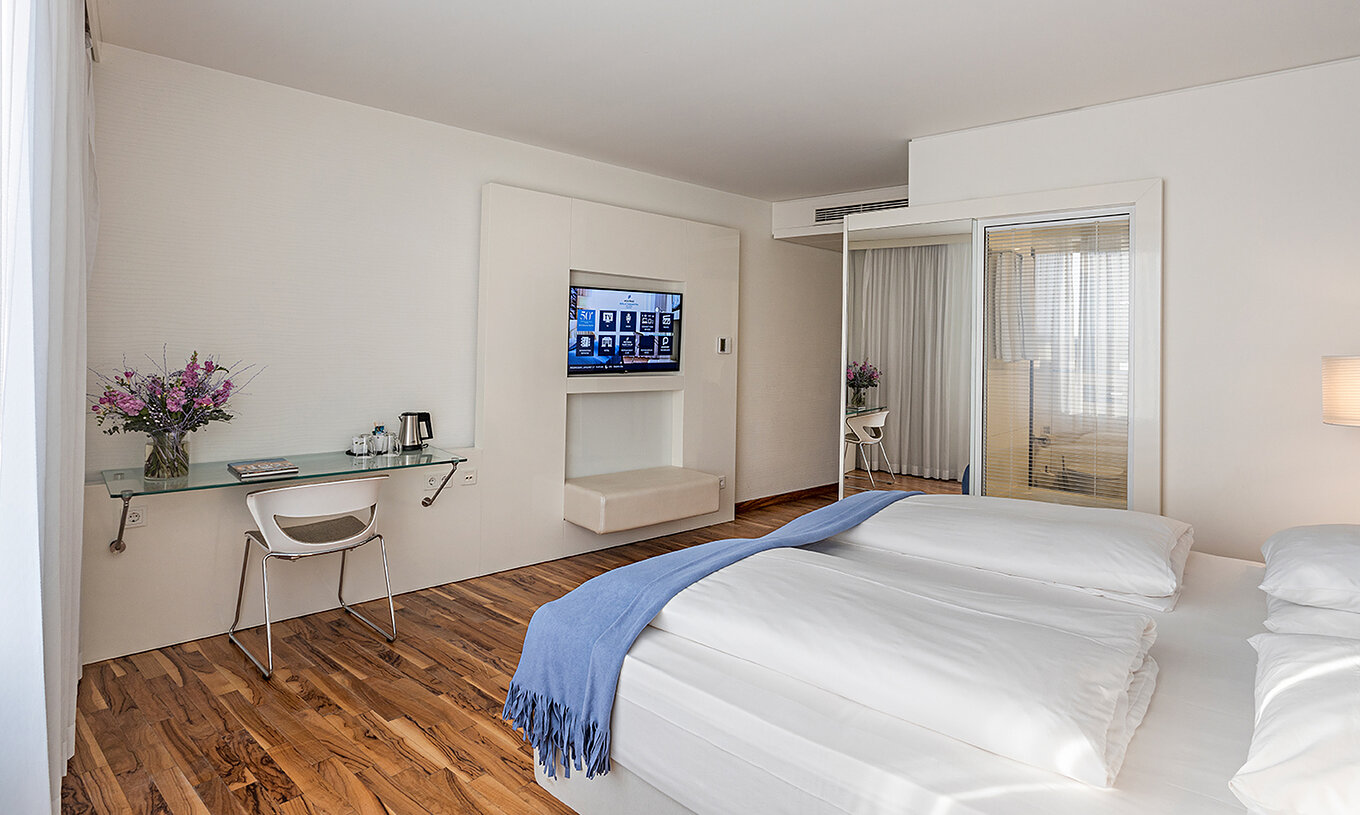 La Chambre Deluxe du Pestana Berlin Tiergarten a une Télévision, un Bureau avec Lampe et Chaise, un Canapé et un Fauteuil