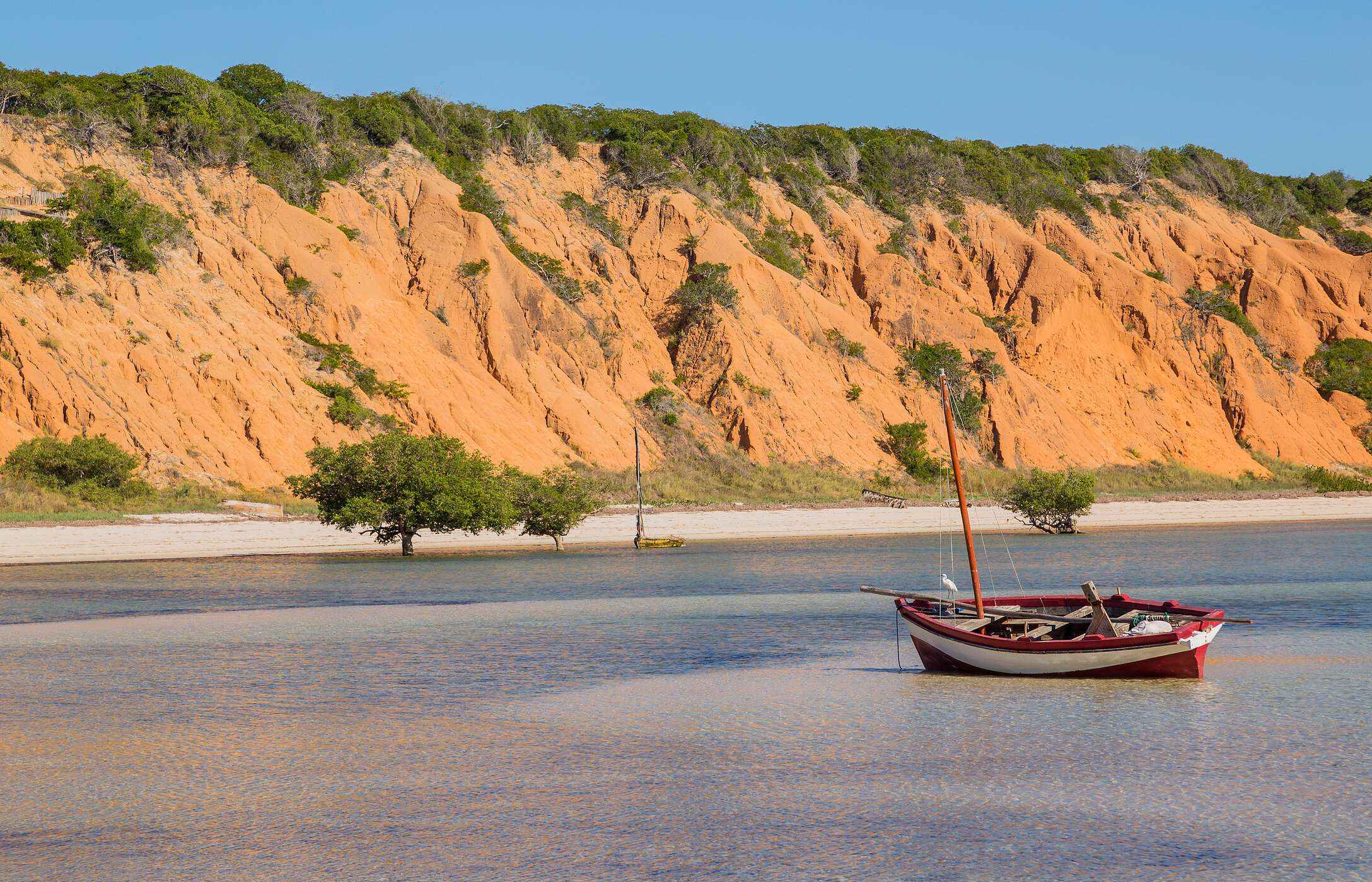 Vue sur la mer depuis l'île de Magaruque avec un bateau traditionnel ancré et des falaises rougeâtres en arrière-plan