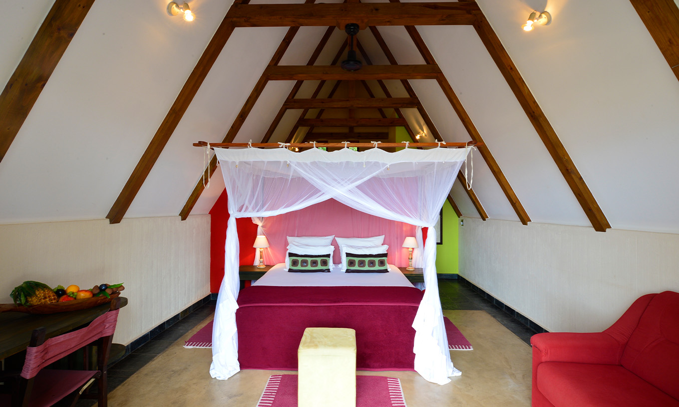 Le Bungalow T1 du Pestana Bazaruto Lodge a un lit double avec baldaquin un canapé et un bureau avec un bol de fruits