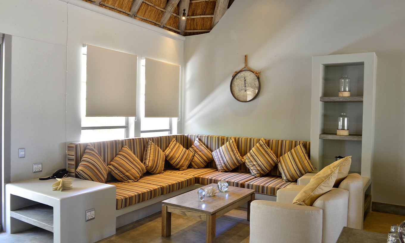 Les Villas T2 du Pestana Bazaruto Lodge ont un canapé en L construit en pierre avec des coussins colorés et deux fauteuils