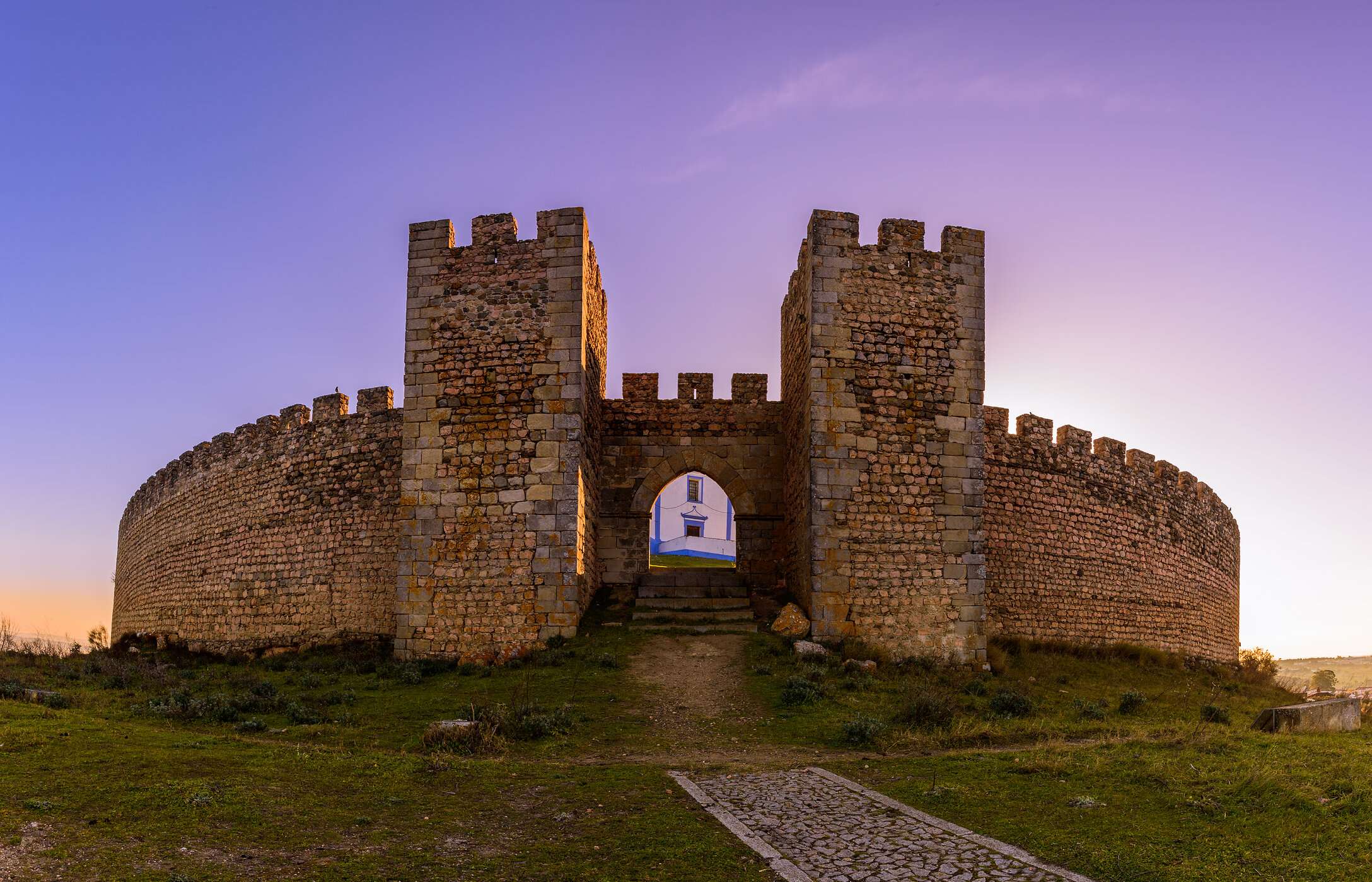 Vue frontale imposante de l'entrée du château d'Arraiolos, avec des murs en pierre et de la végétation autour