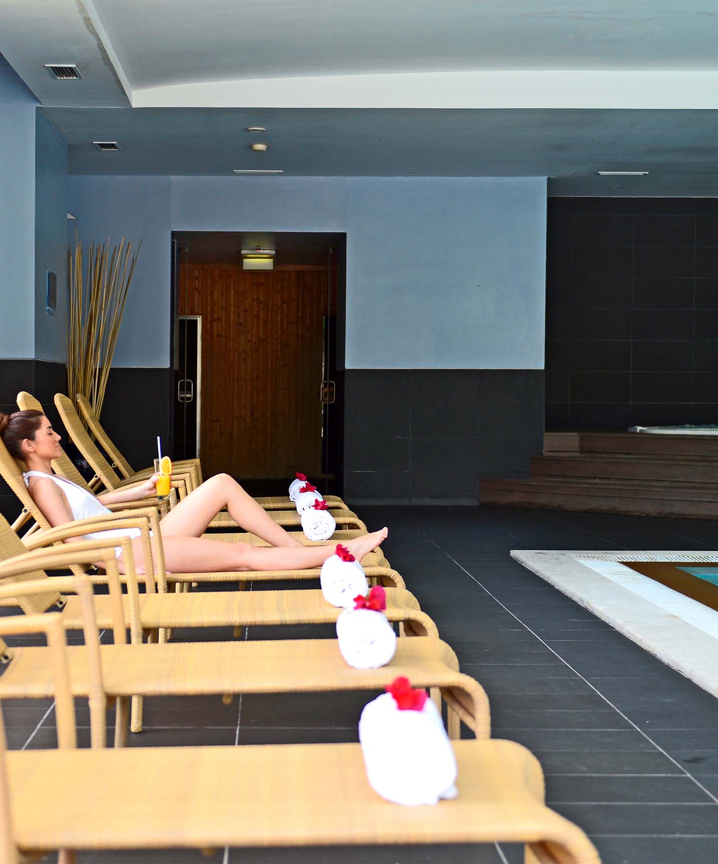 Piscine intérieure avec échelles métalliques et jacuzzi, avec chaises longues et une dame allongée