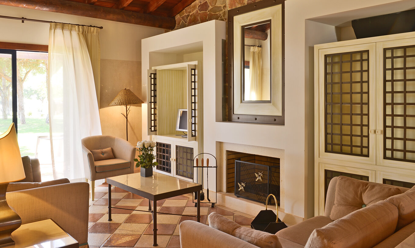 La Suite Vue Jardin Vila Sol du Pestana Vila Sol - Vilamoura avec salon, canapés, table basse, cheminée et fenêtre
