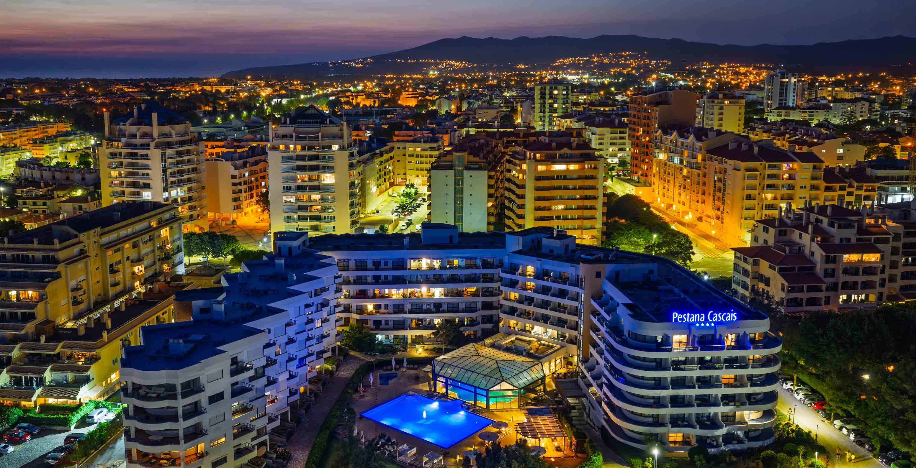 Vue aérienne nocturne du Pestana Cascais et de la ville derrière, tout illuminé avec le ciel orange
